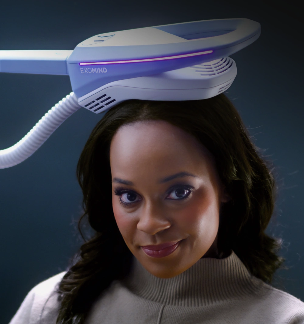 A woman smiles while a Exomind device is placed on her head.
